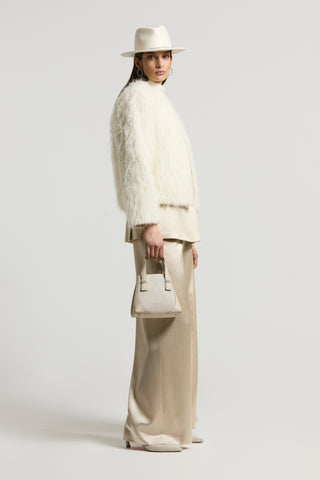 woman with white faux fur jacket simil fil cou, satin beige suit, white fedora hat and beige handbag