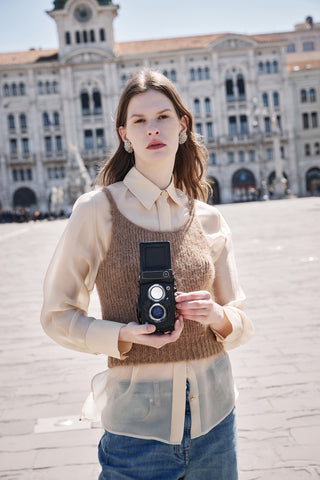 model with beige shirt and camel knitted top with vintage photocamera on hand