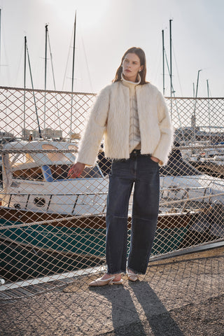 model in front of the boats, wearing denim and a fil coupé white alpaca bomber and a high neck sweater with lurex