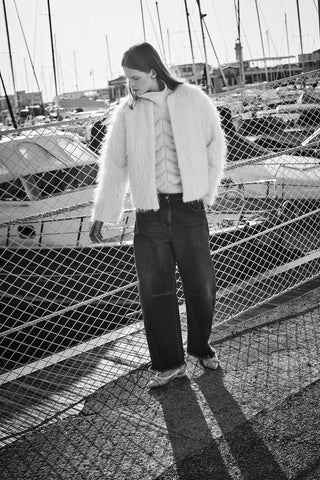 model in front of the boats, wearing denim and a fil coupé white alpaca bomber and a high neck sweater with lurex