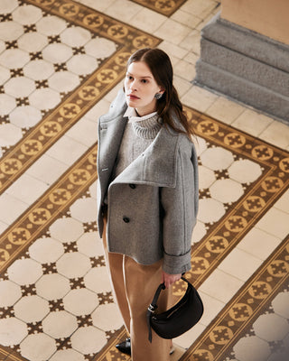 Woman in a gray coat standing on a patterned tiled floor