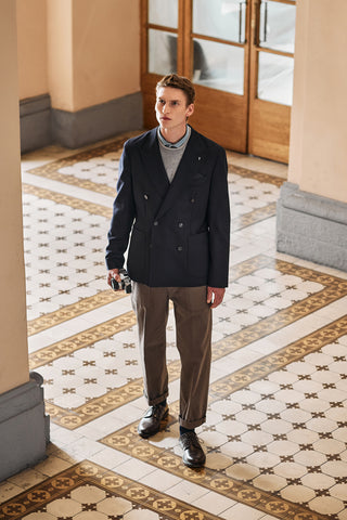 Man in a blue jacket and green trousers standing on a patterned tiled floor