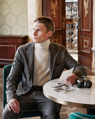 Man sitting at a table in an elegant interior setting, holding a camera and black and white old pictures